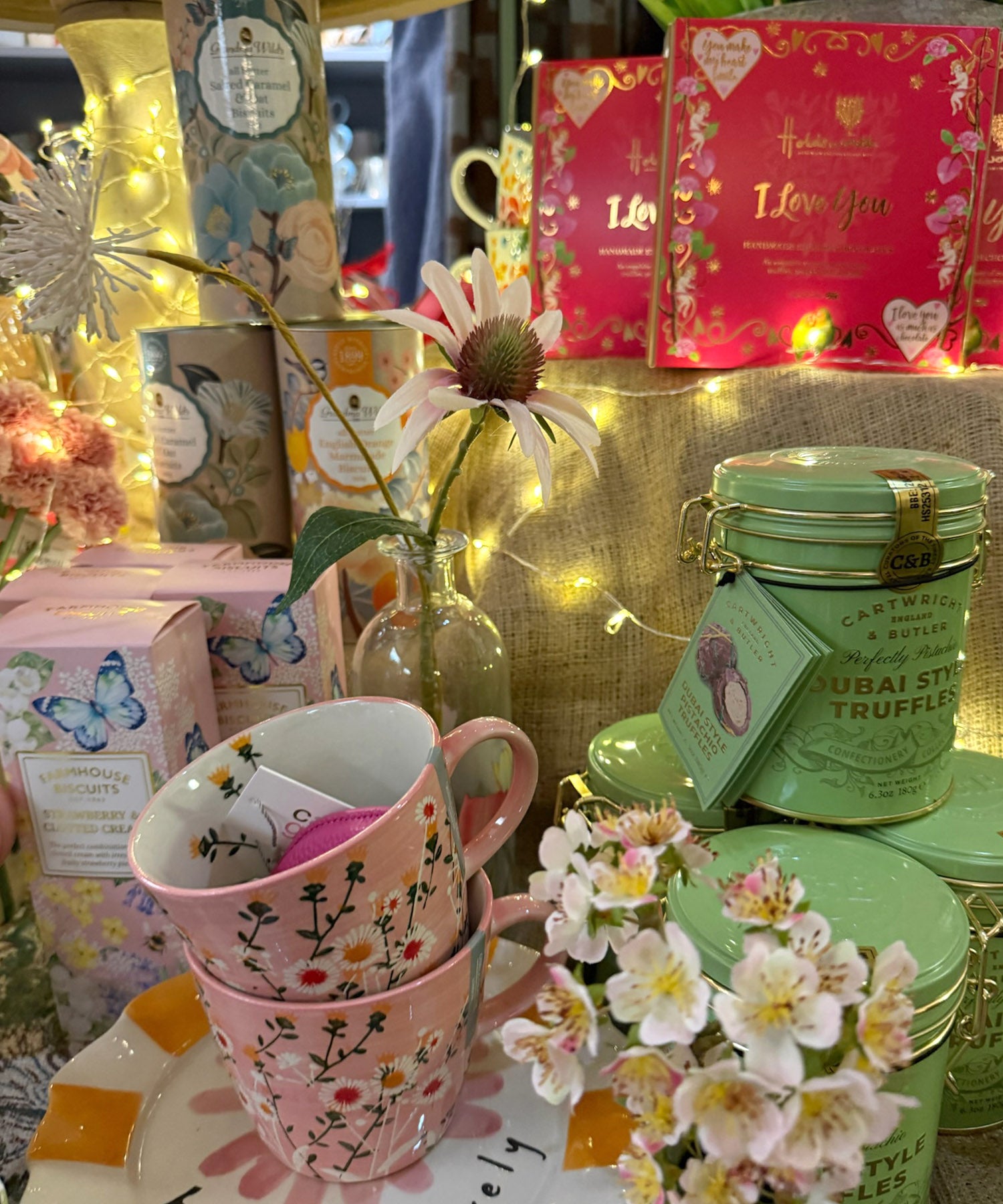 Stack of pink mugs with floral designs, green containers, and decorative items on a table.