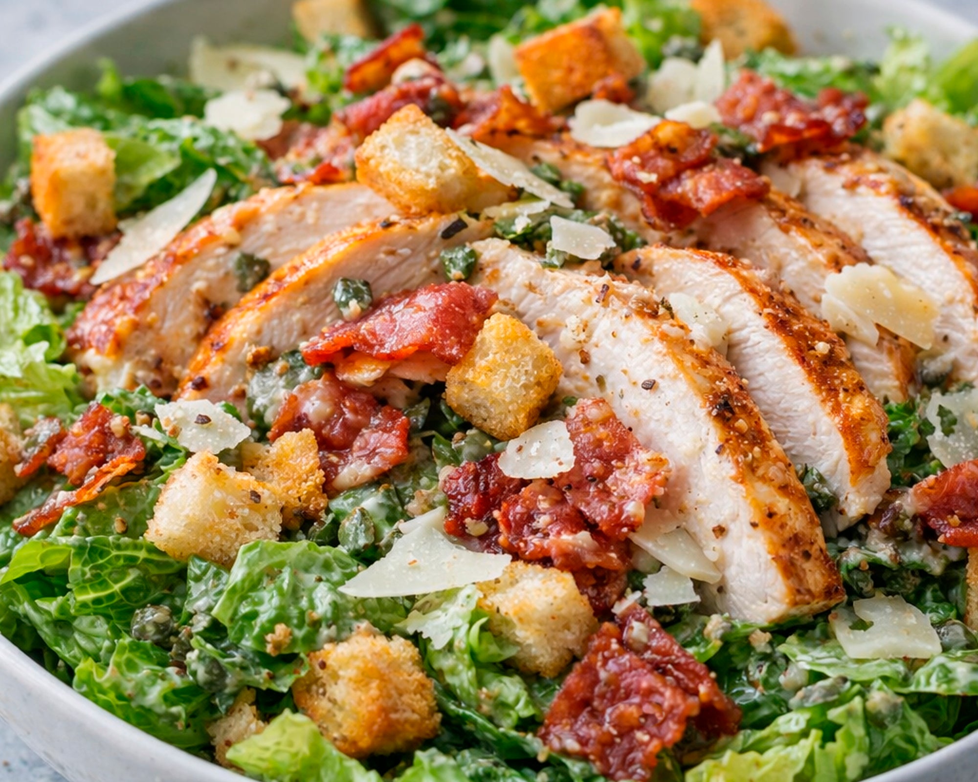 Close-up of a Caesar salad with chicken, bacon, and croutons in a bowl.
