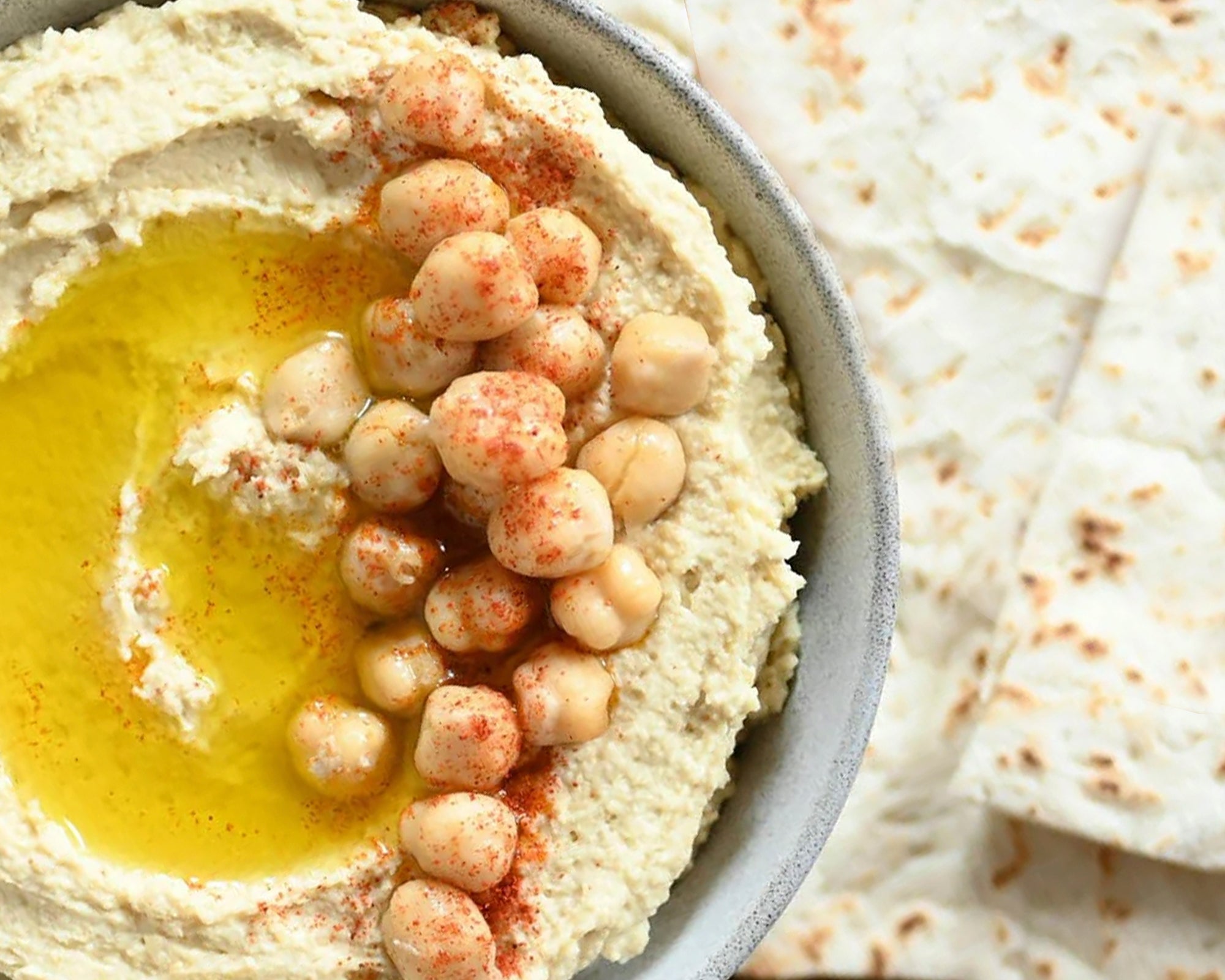 Hummus with chickpeas and olive oil on a plate with flatbread in the background